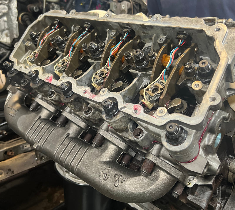 Close-up of a cut-open metal engine block showing internal valve components, wires, and mechanical parts in a workshop setting.