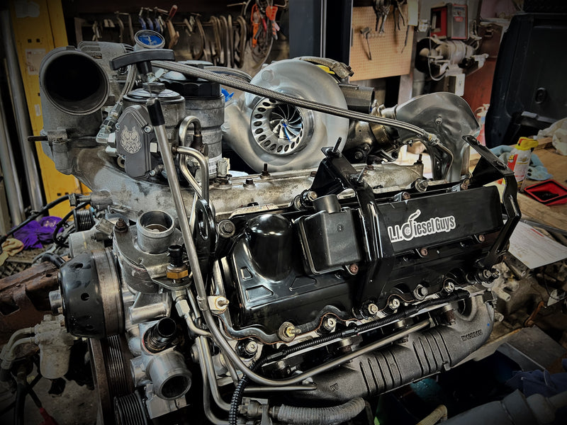 A high-performance diesel engine with a black 'L2 Diesel Guys' valve cover, mounted in a workshop setting.